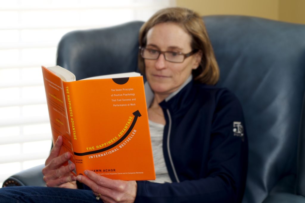 Picture of Kristin reading the book, "The Happiness Advantage" by Shawdn Achor